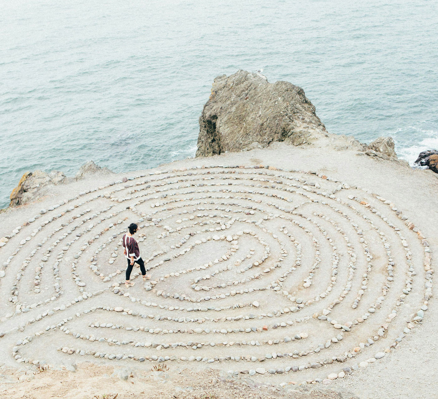 woman walking into a rock maze on a cliff beside the ocean