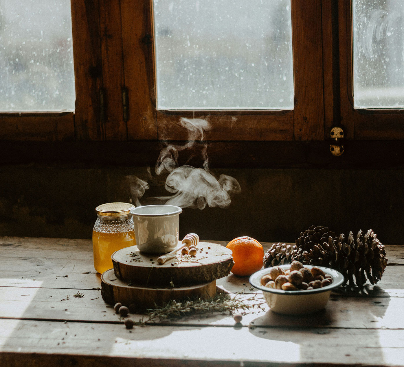 Hot tea with honey surrounded by oranges and pinecones on a rustic wood table